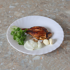 Fried delicious chicken with sliced onions and garlic cloves and sprigs of green parsley on a white plate on the table in the room Selective focus