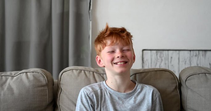 Red hair little boy smiling happy sitting on sofa in living room with 