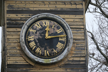 Fototapeta premium Close-up of a round clock face in a wooden tower with peeling paint and gold coloured clock hands and roman numerals in Kent, England, UK.