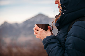 close up tourist drinks tea on a walk in the mountains, a woman stands with a mug in her hands against the background of mountains