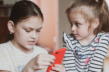 Happy little girls with a smartphone in hands communicate at home with loved ones using modern technology