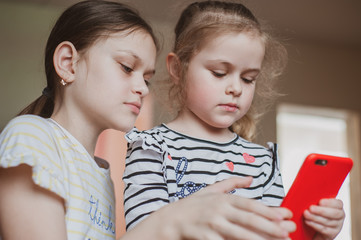 Happy little girls with a smartphone in hands communicate at home with loved ones using modern technology