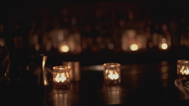 Close up shot of a bar counter in a bar in Bangkok, Thailand. Human drinks a cocktail, candles are burning in the background.