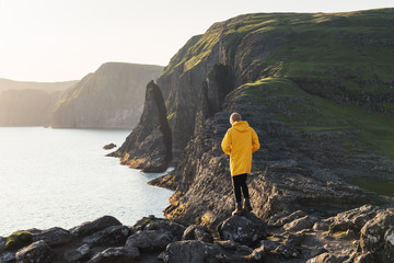 Fototapeta premium Tourist in yellow jacket looks at cliffs near Sorvagsvatn lake on Vagar island, Faroe Islands, Denmark. Landscape photography