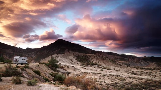 Time lapse of fluffy clouds moving over mountains landscape and caravan vehicle camping on nature in Tabernas desert, Almeria province, Andalusia Spain