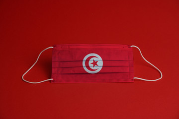 Coronavirus protective mask. Medical mask combined with the Tunisia flag. Red background. Face mask protection against pollution, virus, flu. Healthcare and surgery concept.