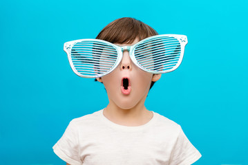 Cheerful little boy in big glasses express a surprised face isolated on blue background