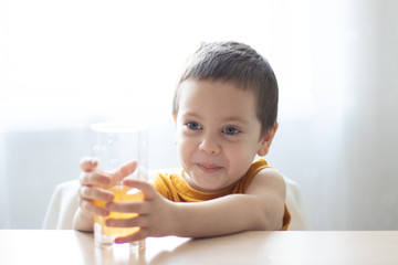 The boy at the table with a glass of juice. the boy wants to drink juice. children's drinks. juice advertisement.