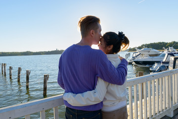 Rear view of young multi ethnic couple kissing each other at the pier outdoors