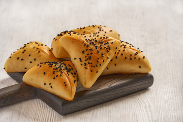 Fatayer samosa with white cheese and black sesame seeds on wooden board.