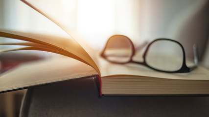 Closeup shot of reading glasses on an open book on a university desk indoors. Close up glasses and open book on the table. Book and glasses on a table in front of couch