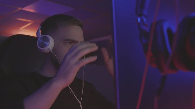 Close up of handsome Caucasian man with beard wearing headphones sitting in front of computer display, playing and then cover face with his palms