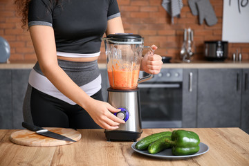 Sporty woman making smoothie in kitchen at home