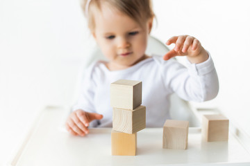 Cute baby girl playing with wooden cubes. Little child building tower. Construction block for kids. Montessori educational method. Selective focus