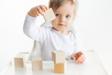 Cute baby girl playing with wooden cubes. Little child building tower. Construction block for kids. Montessori educational method. Selective focus