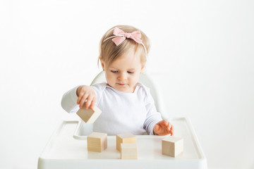 Baby girl playing with wooden cubes by left hand. Playing toddler isolated on white background. Games for kids, preschool education. Close up, selective focus