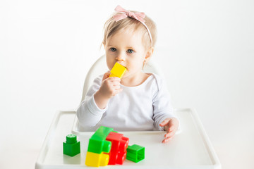 Beautiful blonde baby girl enjoying play with toys at kindergarten, nursery hand shows on colorful blocks. playing toddler isolatd on white background