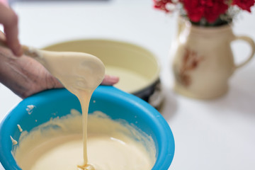Woman hand with wooden spoon stirring raw cake dough at home