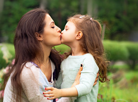 Beautiful mother and cute small daughter kissing on summer green background. Closeup