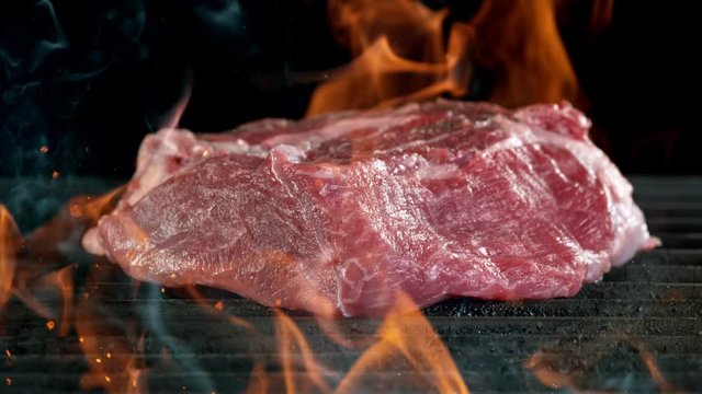 Close-up of falling raw tasty beef steak on iron cast grate, super slow motion, filmed on high speed cinematic camera at 1000 fps.