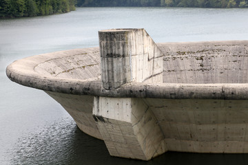 Close-up of big overflow concrete funnel above the lake water surface .