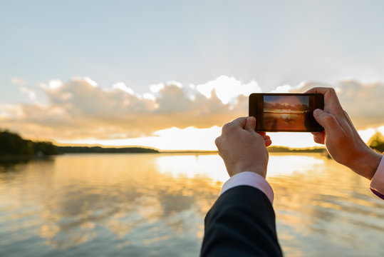 Hands of young man taking pictures with phone of beautiful sunset