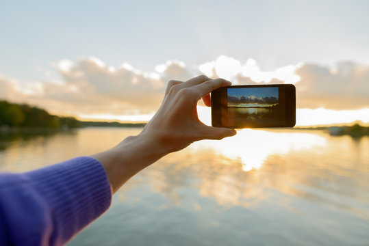 Hands of young man taking pictures with phone of beautiful sunset