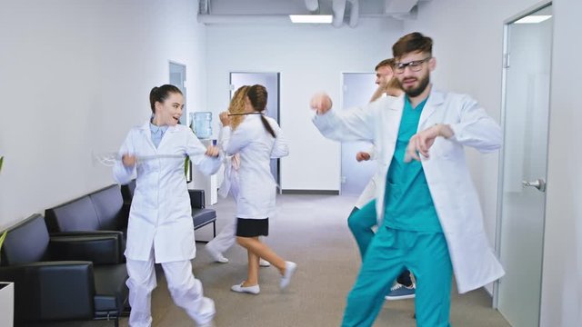 In a modern hospital corridor group of funny dancing doctors and nurses dancing and have fun