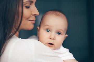 Close-up portrait of a serene cute beautiful baby boy on hands of happy smiling mother. Healthcare and medical love woman mother's day concept.