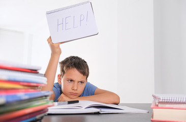 Upset tired preteen child sitting at the table, doing his homework among pile of books. Word Help...