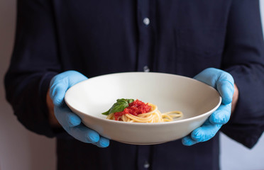 Home delivery food from the restaurant during a pandemic. Italian food delivery. Man or chef holding plate with spaghetti