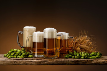 four glasses of light beer for a company with hops and wheat on a wooden table