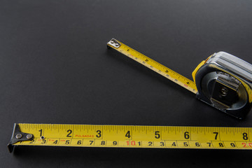 Flexometro o metro color plata con la cinta metrica amarilla sobre un fondo de color negro