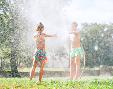 Two kids, brother and sister, play with watering hose in summer garden
