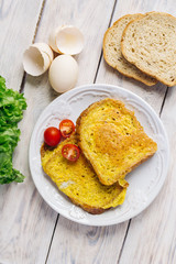 French toast, fried in eggs, lies in a white plate on a light wooden rustic table