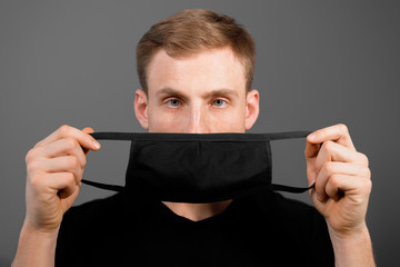 Handsome man in black t-shirt wear black medical mask, gray background. Coronavirus covid-19...