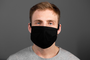 Handsome man in black t-shirt wear black medical mask, gray background. Coronavirus covid-19...