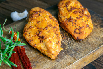 Spicy baked chicken breast with peper, rosemary an garlic on wooden cutting board on wooden table....