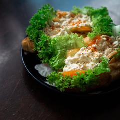 Chicken salad in croissant bun with a healthy salad leaves and tomatoes on a dark, wooden background.
