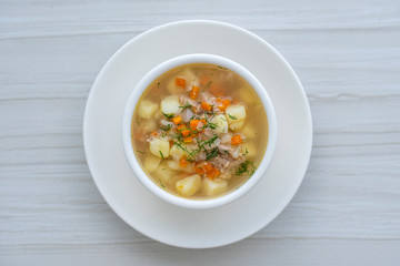 Fresh fish soup with carrots, potatoes and onions in a white plate, close up. Tasty dinner consists of a fish soup with tuna