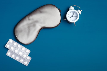 Healthy sleeping and insomnia treatment concept. Sleep eye mask, alarm clock, sleeping pills on...
