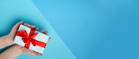 Obraz premium White woman holding a white gift box with a red bow on a blue one . Gift for birthday, Christmas, Valentine's Day, New year . Flat lay