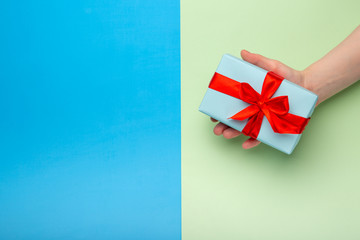 Woman holds a white gift box with a red bow on a colored background. Gift for birthday, Christmas, Valentine's Day, New year . Flat lay
