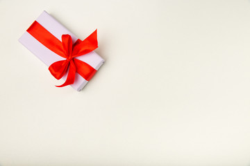 Holiday gift box with a red ribbon bow isolated on a beige background.