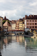 Fototapeta na wymiar Flower-bedecked bridge with view of the Île palace (former prison) home to the Annecy History museum, Thiou canal, Île quayside and houses with colourful facades.