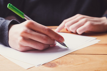 young woman hands writing notes on sheet of paper with pen closeup, wooden table, female student