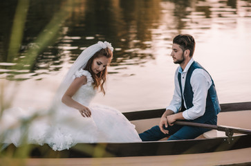 young beautiful newlywed couple sit in wooden white boat