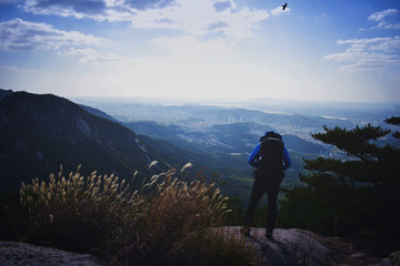 A lone mountain hiker set against the blue tinted  Korean landscape adjusts the front of his hiking pack. Taken at Bukhansan Mountain in South Korea. 