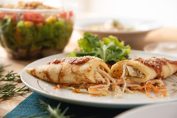 Chicken pancake on top of a white plate on a wooden table with salads in the background. Brazilian pancake