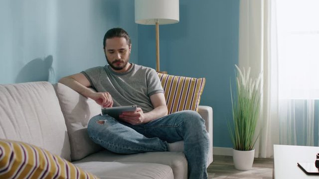 Young man stays home, uses his gadget to navigate the Internet, spending time online, looking for news in social media, slow motion.